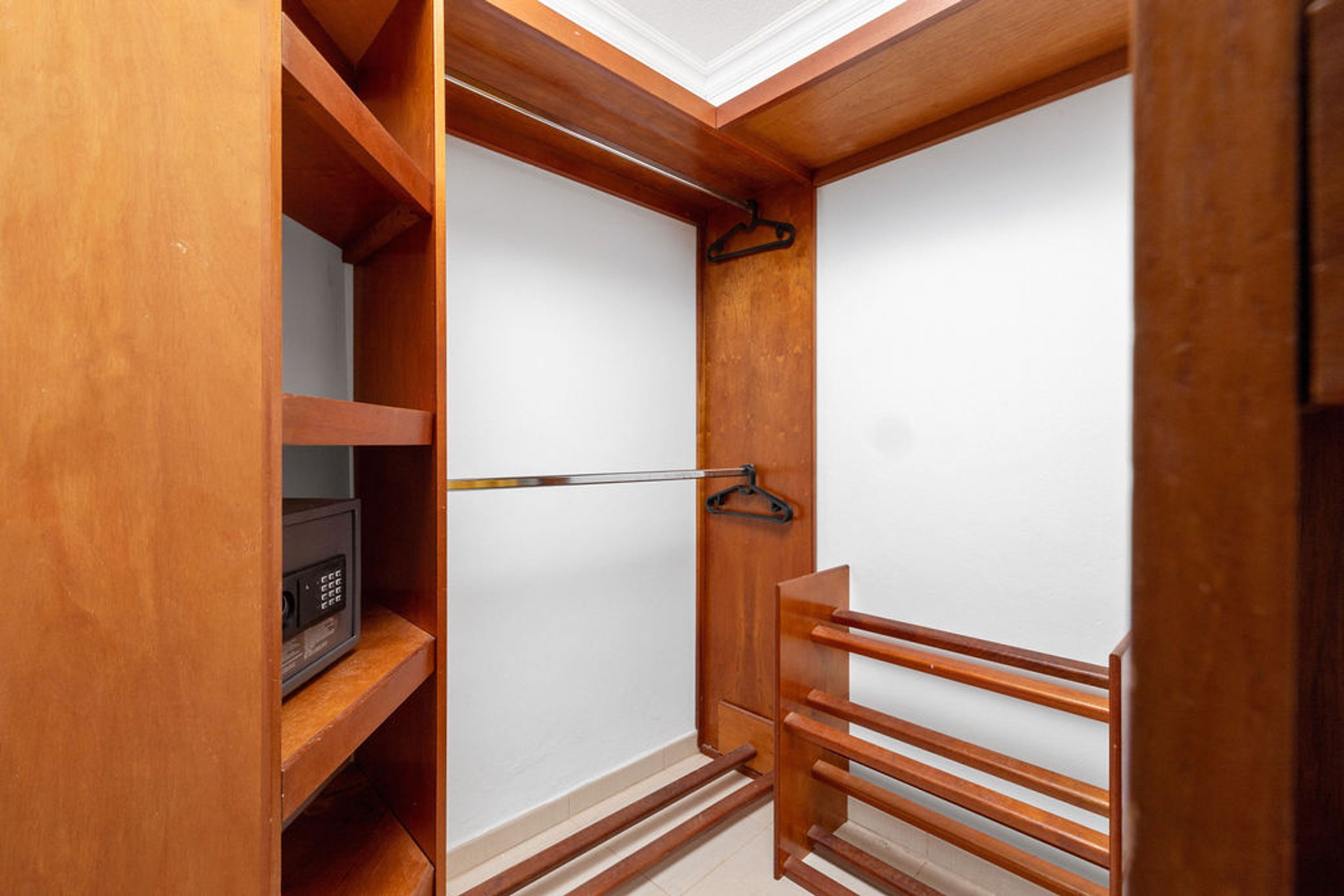 A walk-in closet with wooden shelving, a hanging rod, and a microwave.