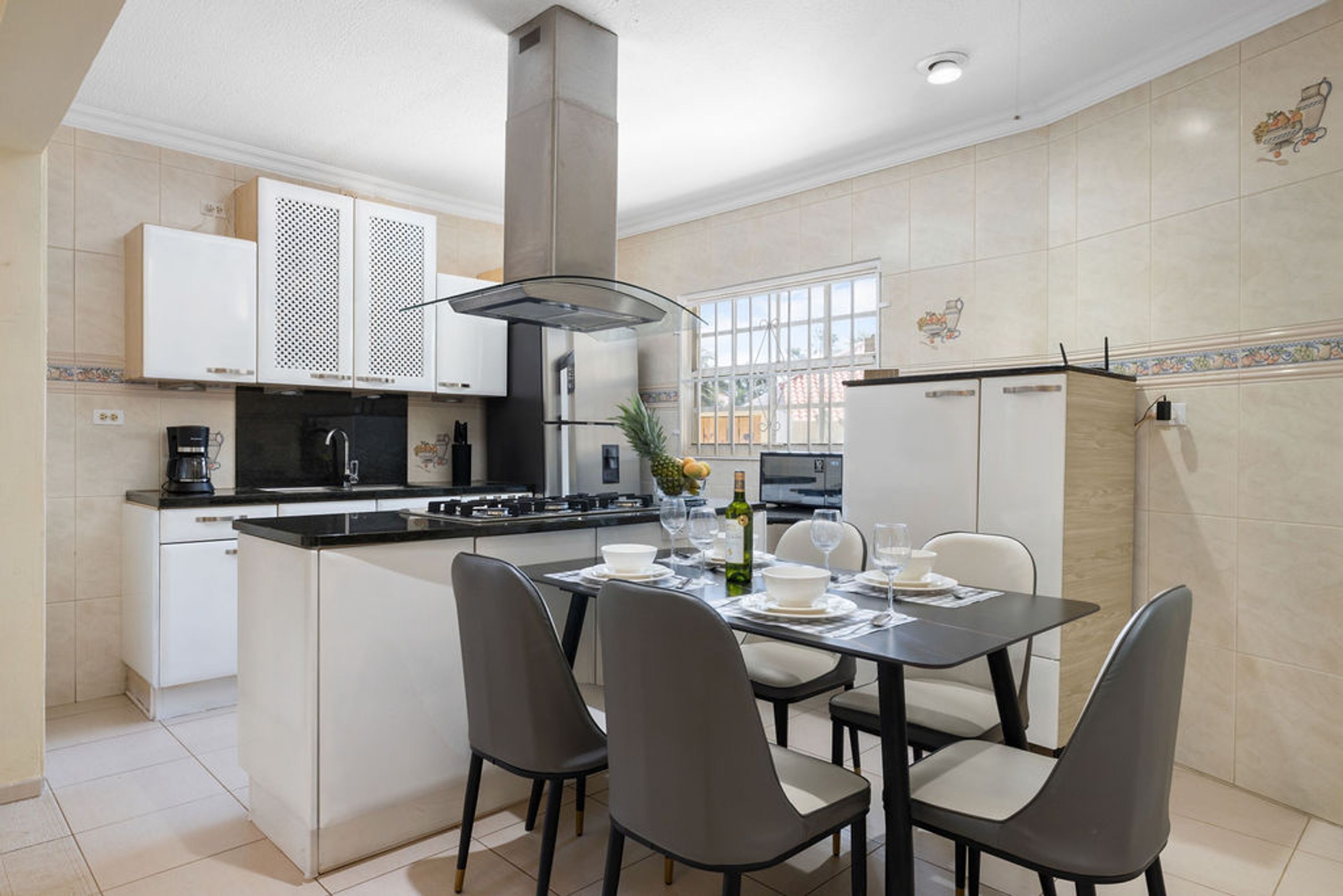A modern kitchen with a central island, white cabinets, and a dining area with chairs and a table set for two.