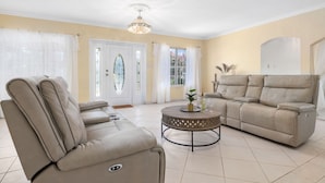 Una sala de estar con un sofá color beige, un sillón reclinable y una mesa de centro redonda.