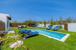 A backyard with a swimming pool, blue lounge chairs, and a wooden fence.