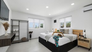 A modern bedroom with a bed, bedside table, TV, and a wardrobe. - 2BR Countryside Home w Sea Views Private Pool (Noord)