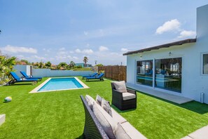 Uma casa moderna com piscina, um terraço com espreguiçadeiras e uma porta de vidro que dá para uma área externa coberta.