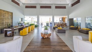 Un vestíbulo amplio con una mesa de centro de madera, asientos de color amarillo y blanco, y un mostrador de recepción.