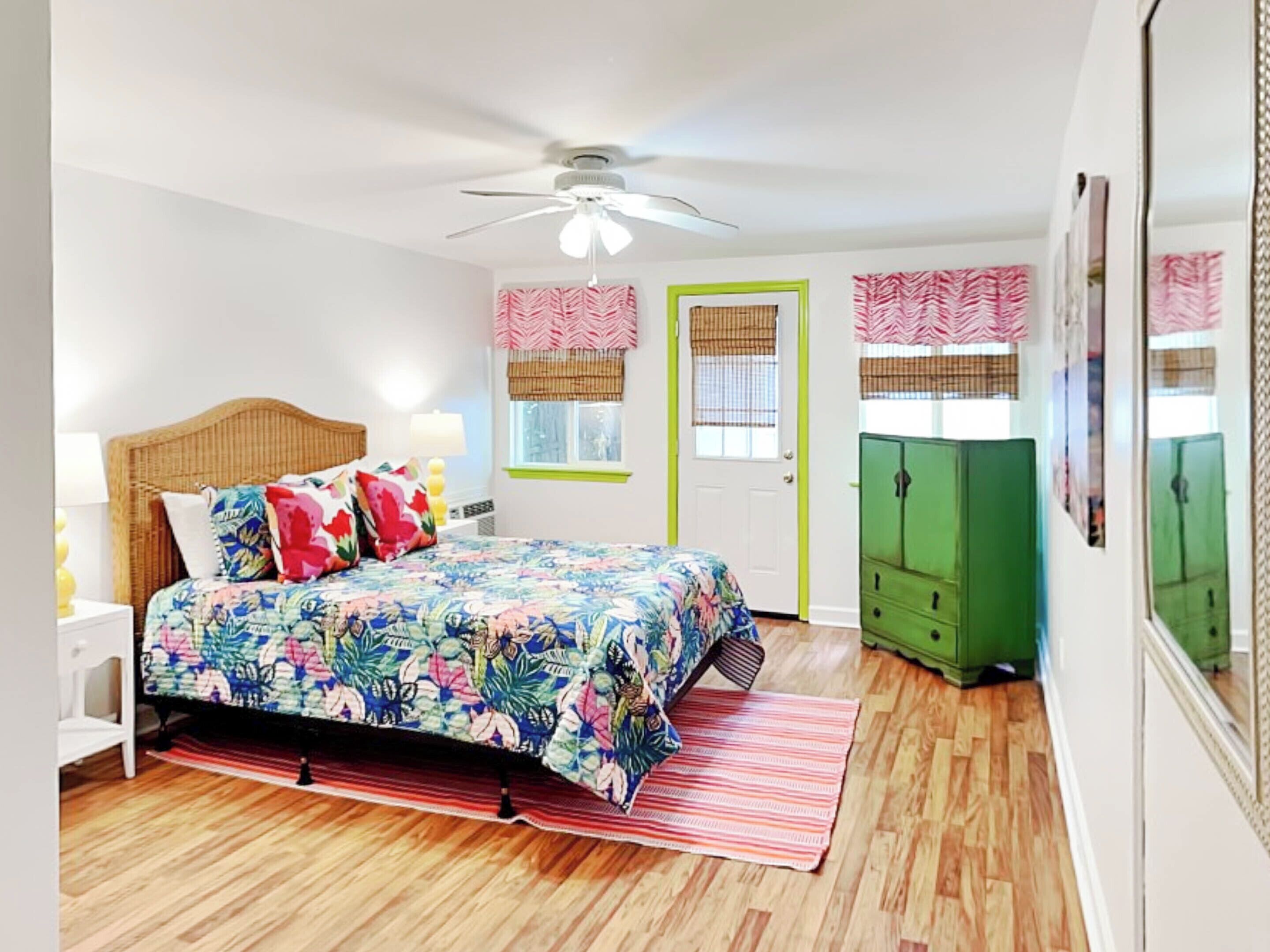 A bedroom with a bed, a nightstand, a green wardrobe, a ceiling fan, and a window with a view.