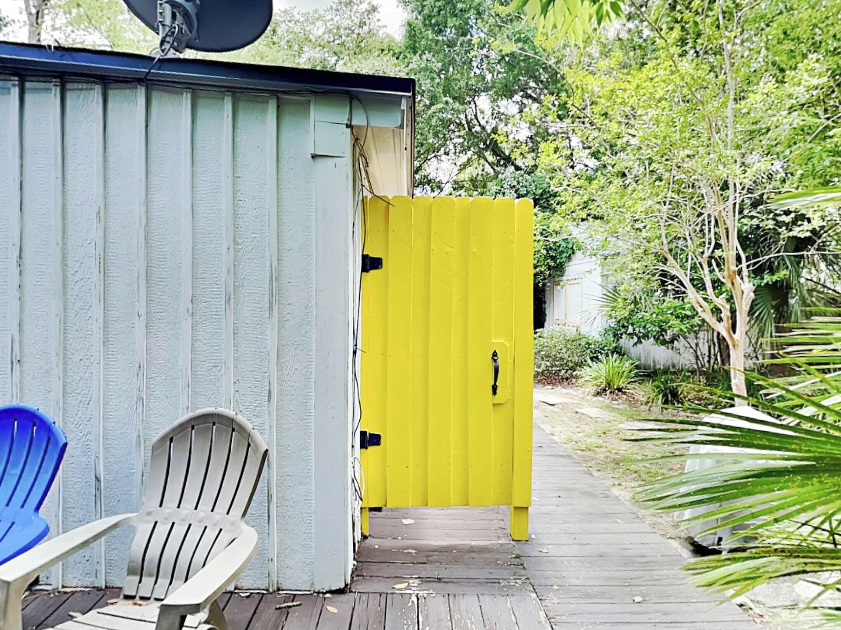 A small, enclosed outdoor area with a yellow door, a white chair, and a blue chair.