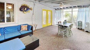 A room with a blue sofa, a dining table with chairs, a yellow door, and a fish decoration on the wall. - A Shore Thing by Tybee Vacation Rentals (Tybee Island)