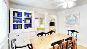 A dining area with a wooden table and black chairs, a white cabinet with blue shelves, and a wall-mounted sign reading "SEAFOOD". - A Shore Thing by Tybee Vacation Rentals (Tybee Island)