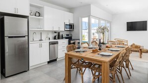 Eine moderne Küche mit weißen Schränken, Edelstahlgeräten und einem Essbereich mit einem Holztisch und Korbstühlen.