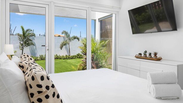 Ein Schlafzimmer mit einem großen Bett, einem an der Wand befestigten Fernseher und einer Glastür, die zu einem Garten führt.