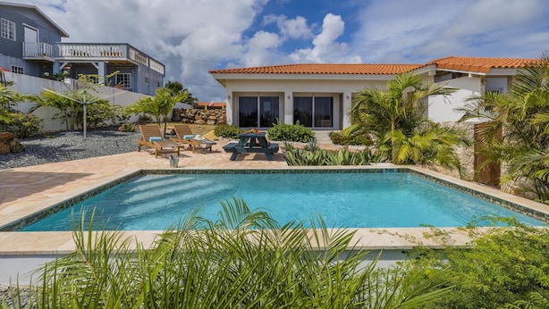 A swimming pool with lounge chairs and a patio area surrounded by tropical plants. - Breezy Cozy Retreat Arikok National Park Pool (Santa Cruz)