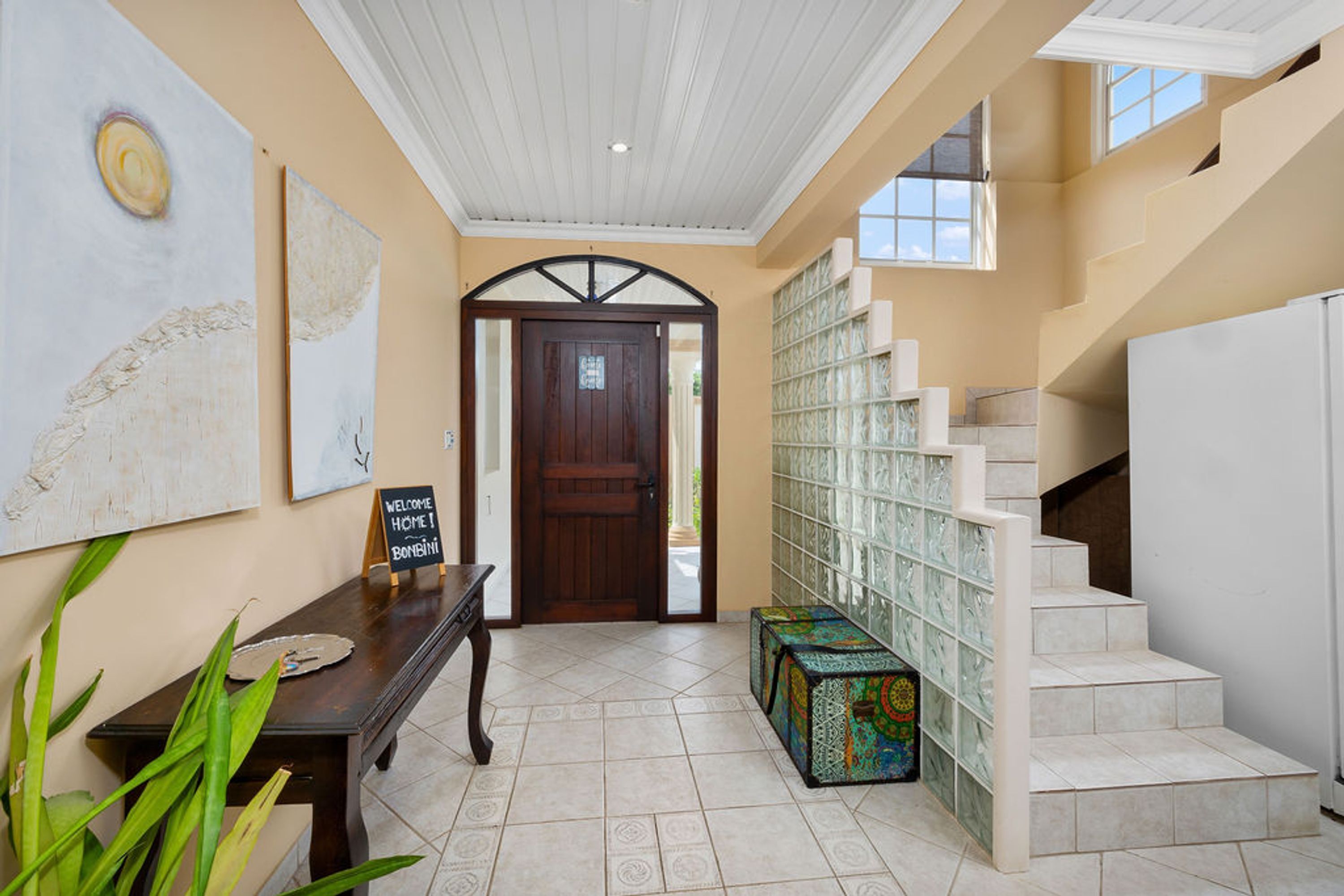 A reception area with a wooden bench, a welcome sign, a door, and a staircase with a patterned wall.
