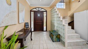 A reception area with a wooden bench, a welcome sign, a door, and a staircase with a patterned wall.