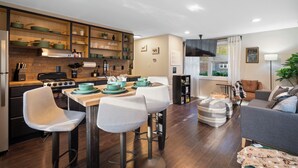 A modern kitchen with a dining area, wooden flooring, and a sofa in a living room. - Creekside Cabin: Hot Tub, Cinema, EV Charger, Dogs (Luray)