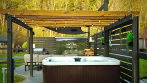 An outdoor patio area with a hot tub, a grill, and a pergola. - Creekside Cabin: Hot Tub, Cinema, EV Charger, Dogs (Luray)