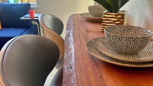 A wooden dining table with a woven plate and a potted plant. - Tropical Oasis (Quail heights)