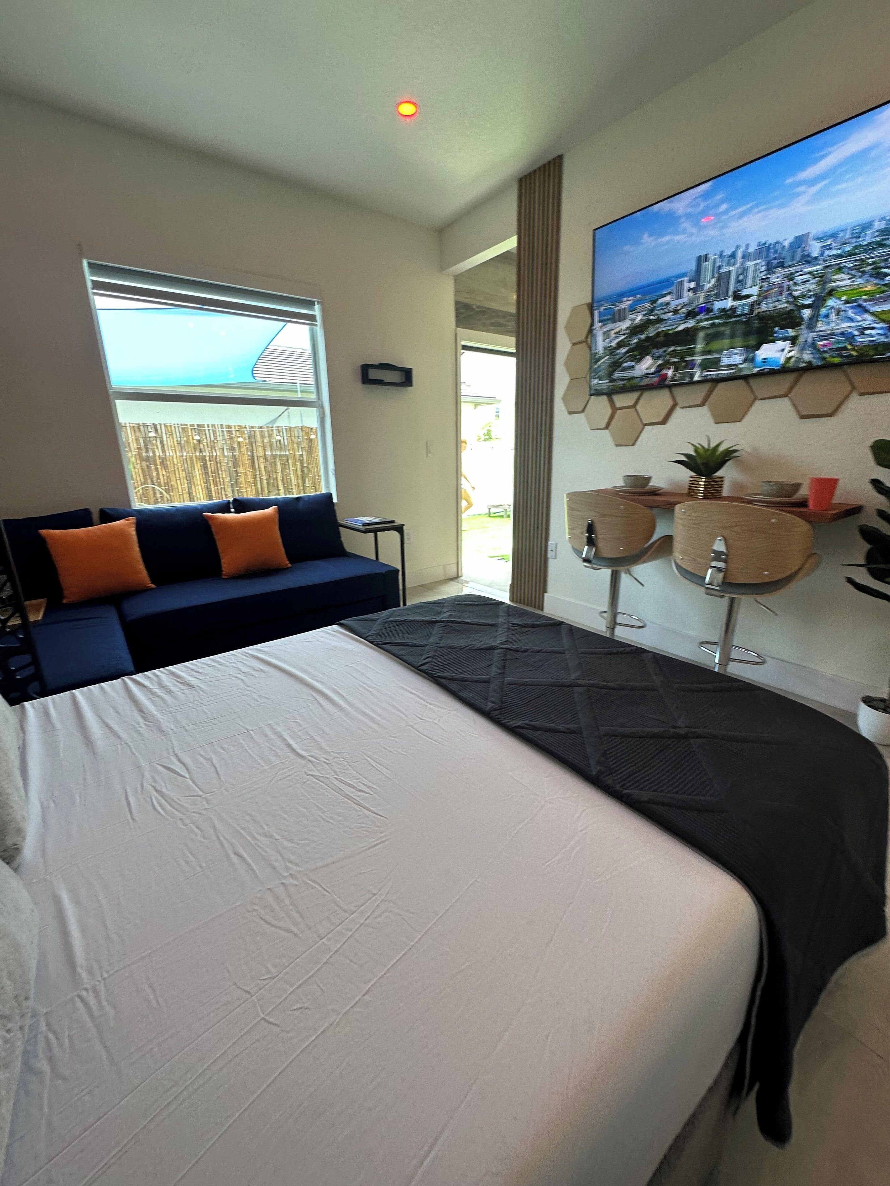 A modern hotel room with a large bed, a sofa, a TV mounted on the wall, and a view of the city through the window.