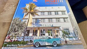 A book titled 'Miami' with a cover image of a building and a car, placed on a wooden table. - Tropical Oasis (Quail heights)