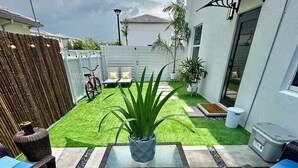 A patio area with a glass-top table, wicker chairs, and a small potted plant. - Tropical Oasis (Quail heights)