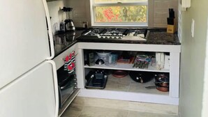 A compact kitchen with a built-in stove, white cabinetry, and a window with a view of foliage. - Country Road, Take me Home- your own Island Cottage! (Savannah)