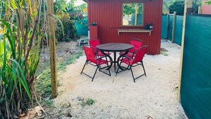 A covered outdoor area with a red building, a round table with red chairs, and a bar counter. - Country Road, Take me Home- your own Island Cottage! (Savannah)
