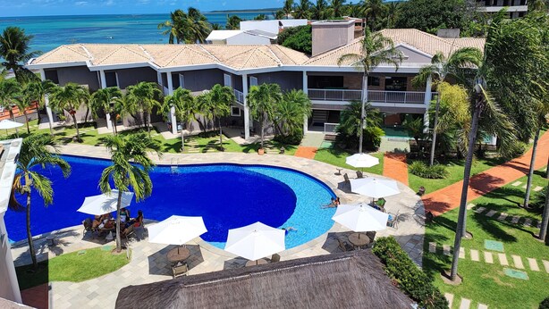 A resort with a large swimming pool, outdoor seating, and a view of the ocean. - Hotel Coral Beach  (Tamandaré)