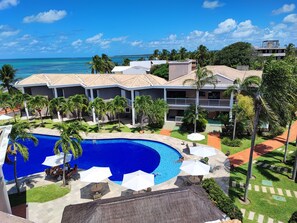A resort with a large swimming pool, outdoor seating, and a view of the ocean. - Hotel Coral Beach  (Tamandaré)