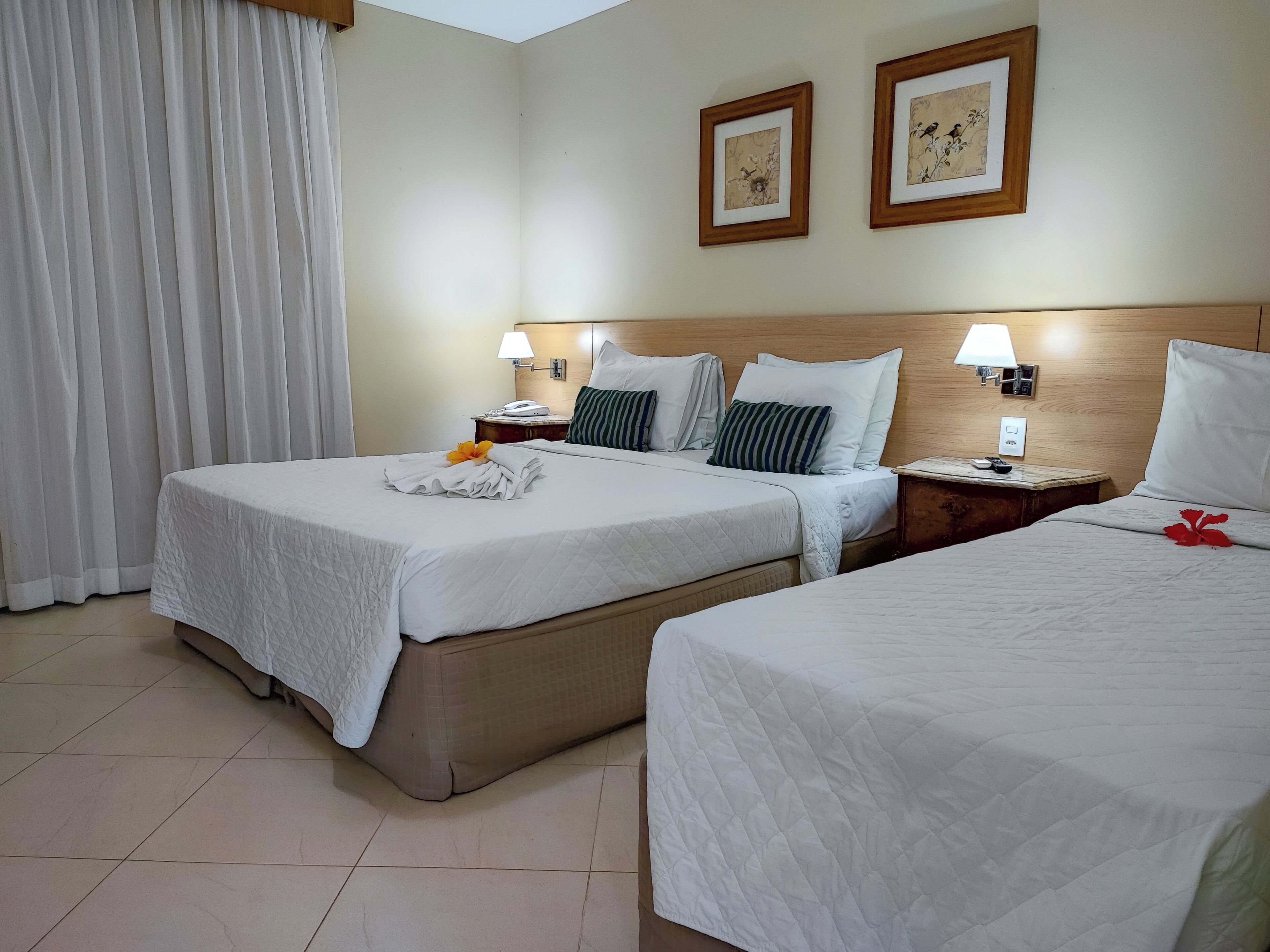 A hotel room with two beds, white bedding, a wooden headboard, a nightstand with a lamp, and two framed pictures on the wall.