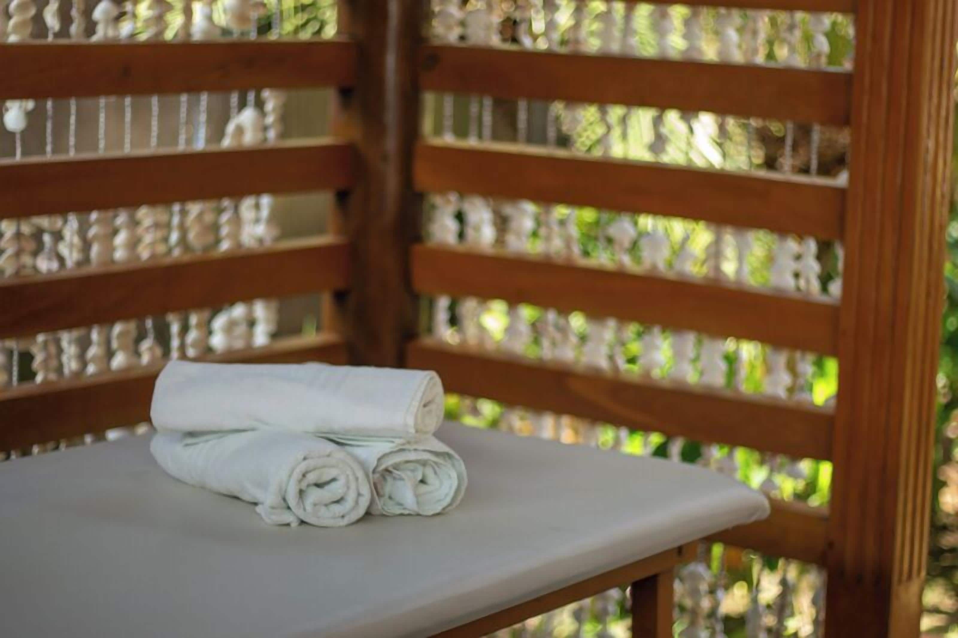 A wooden bench with a white towel rolled up on it, set against a wooden lattice structure.