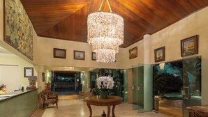 A lobby with a chandelier, a reception desk, and framed pictures on the walls. - Hotel Coral Beach  (Tamandaré)