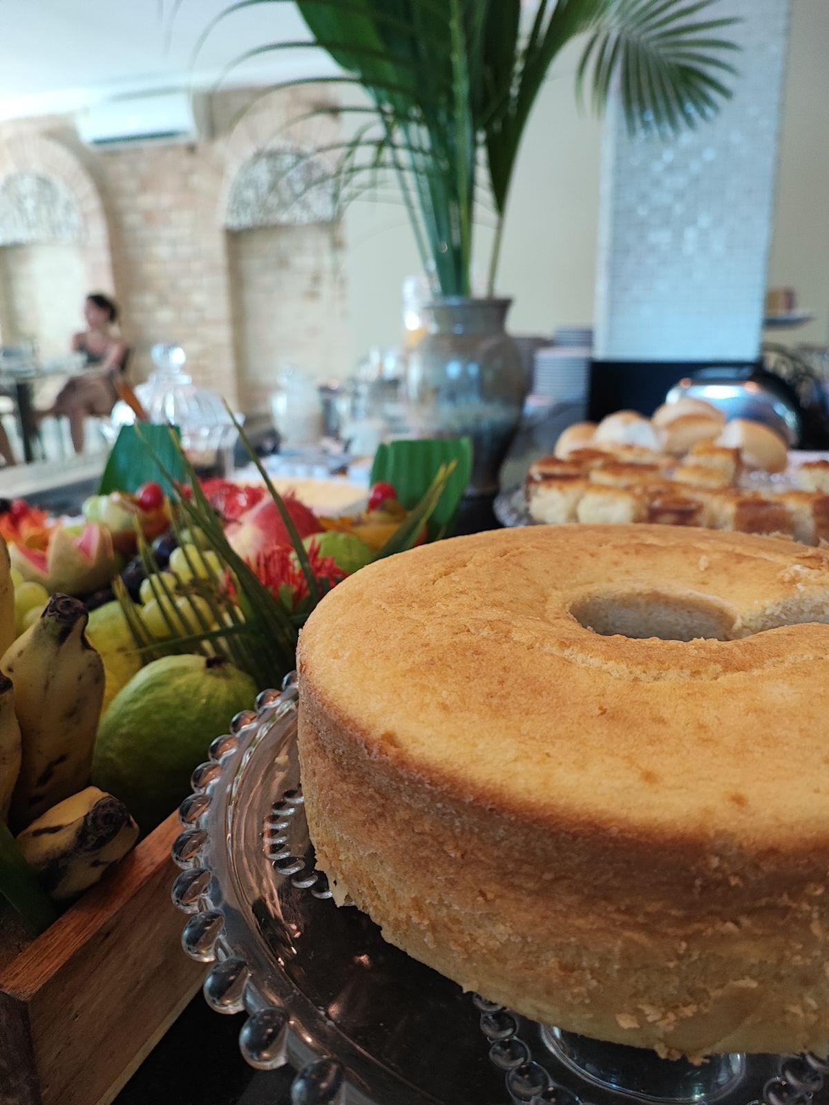 Un pastís sobre un suport de vidre amb una composició de fruita tropical a prop.