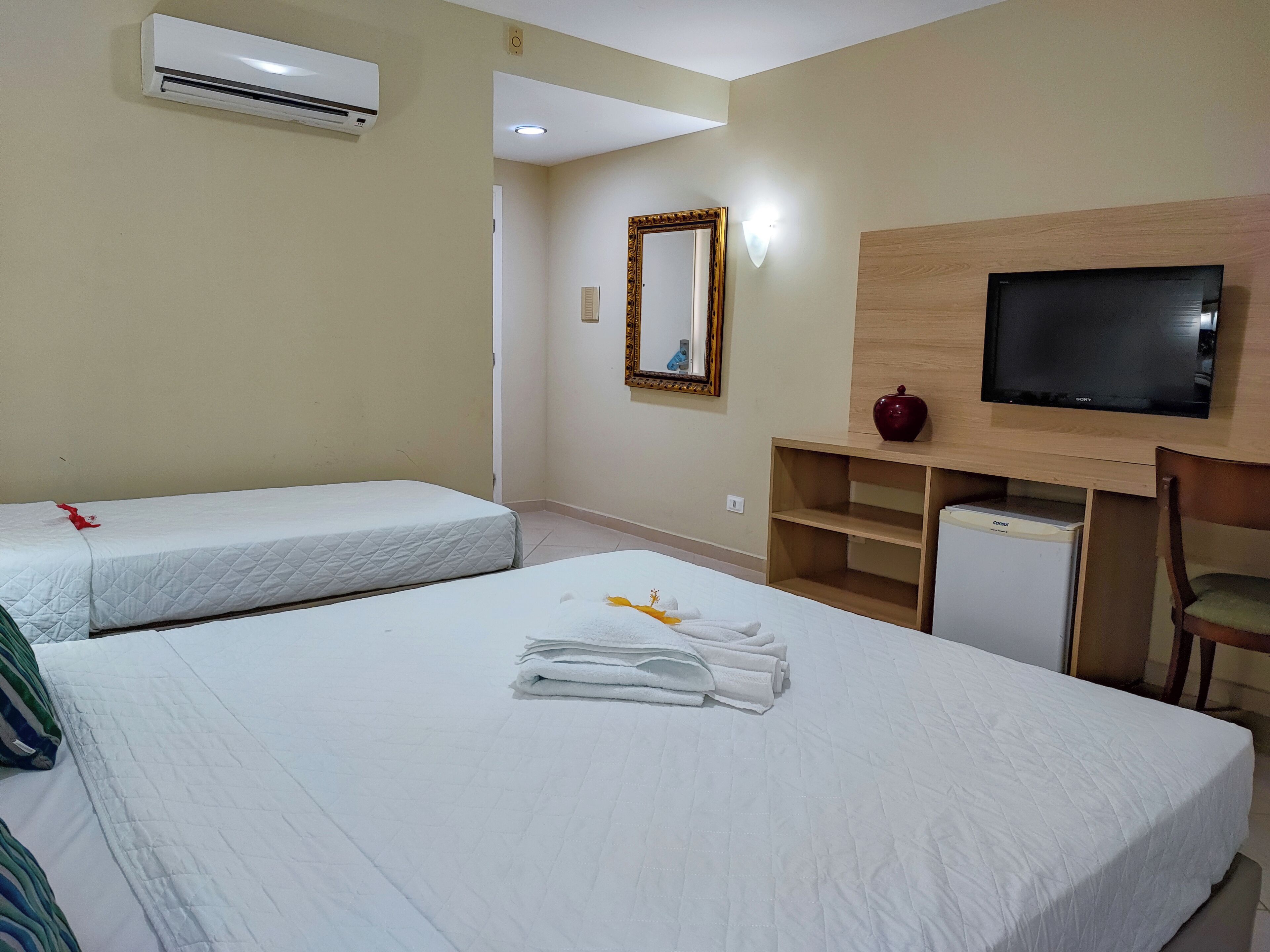 A hotel room with two single beds, a flat-screen TV, a small desk with a chair, and a minibar.