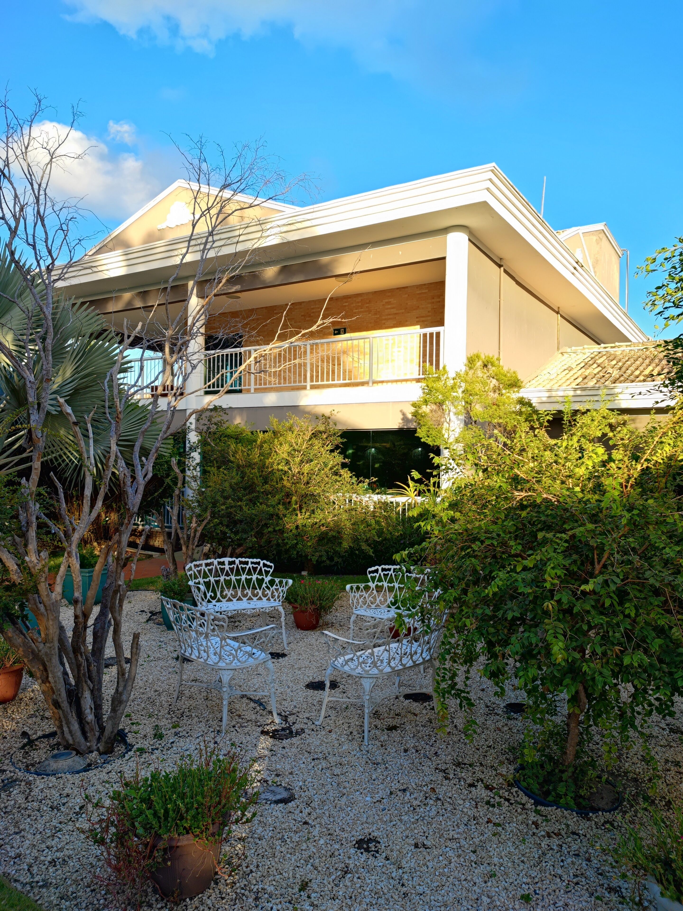 A two-story building with a balcony, surrounded by gravel and potted plants.