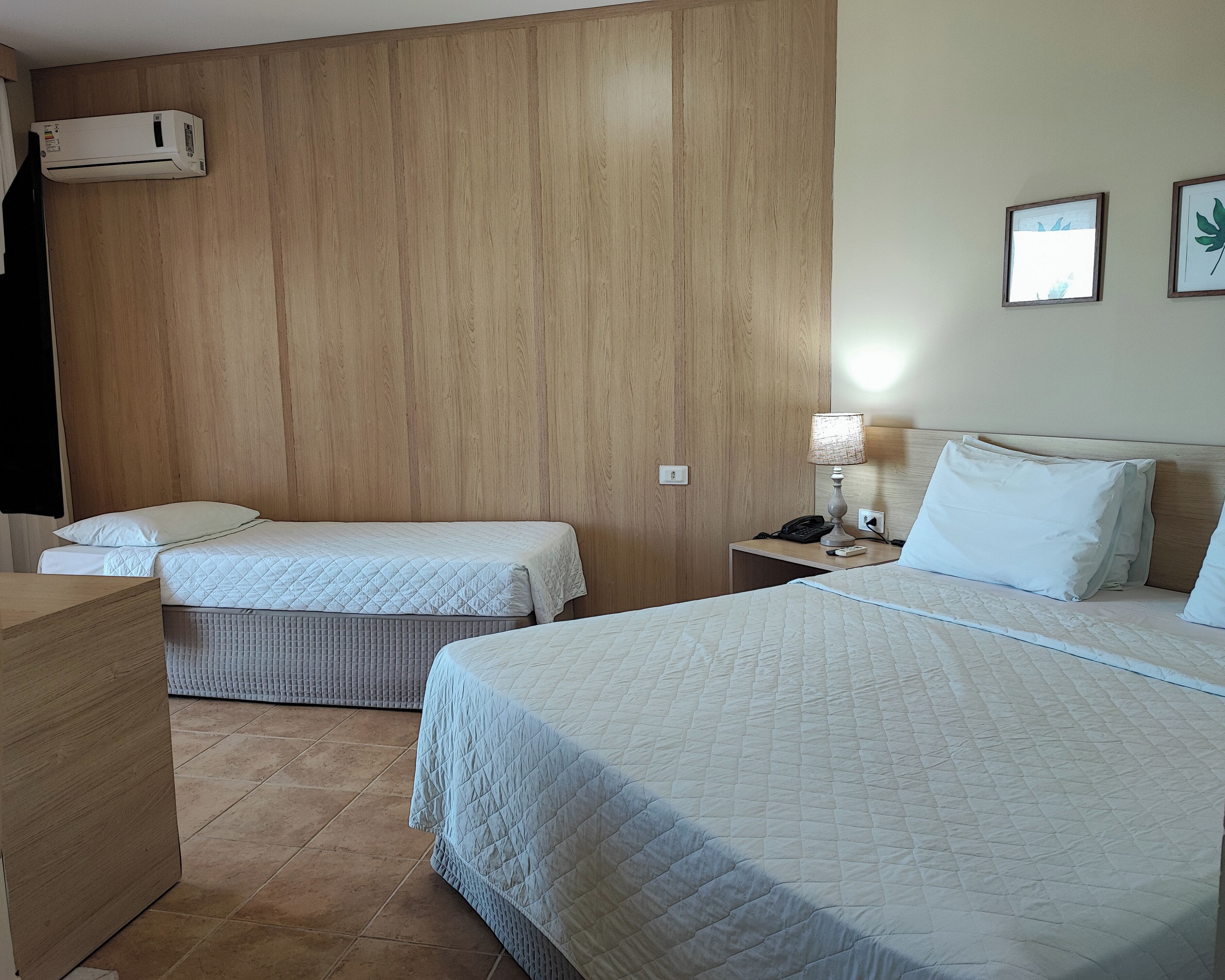 Ein Hotelzimmer mit zwei Betten, einer Wandverkleidung aus Holz, einer Wand-Klimaanlage, einer Nachttischlampe und einem Nachttisch mit Telefon und Lampe.