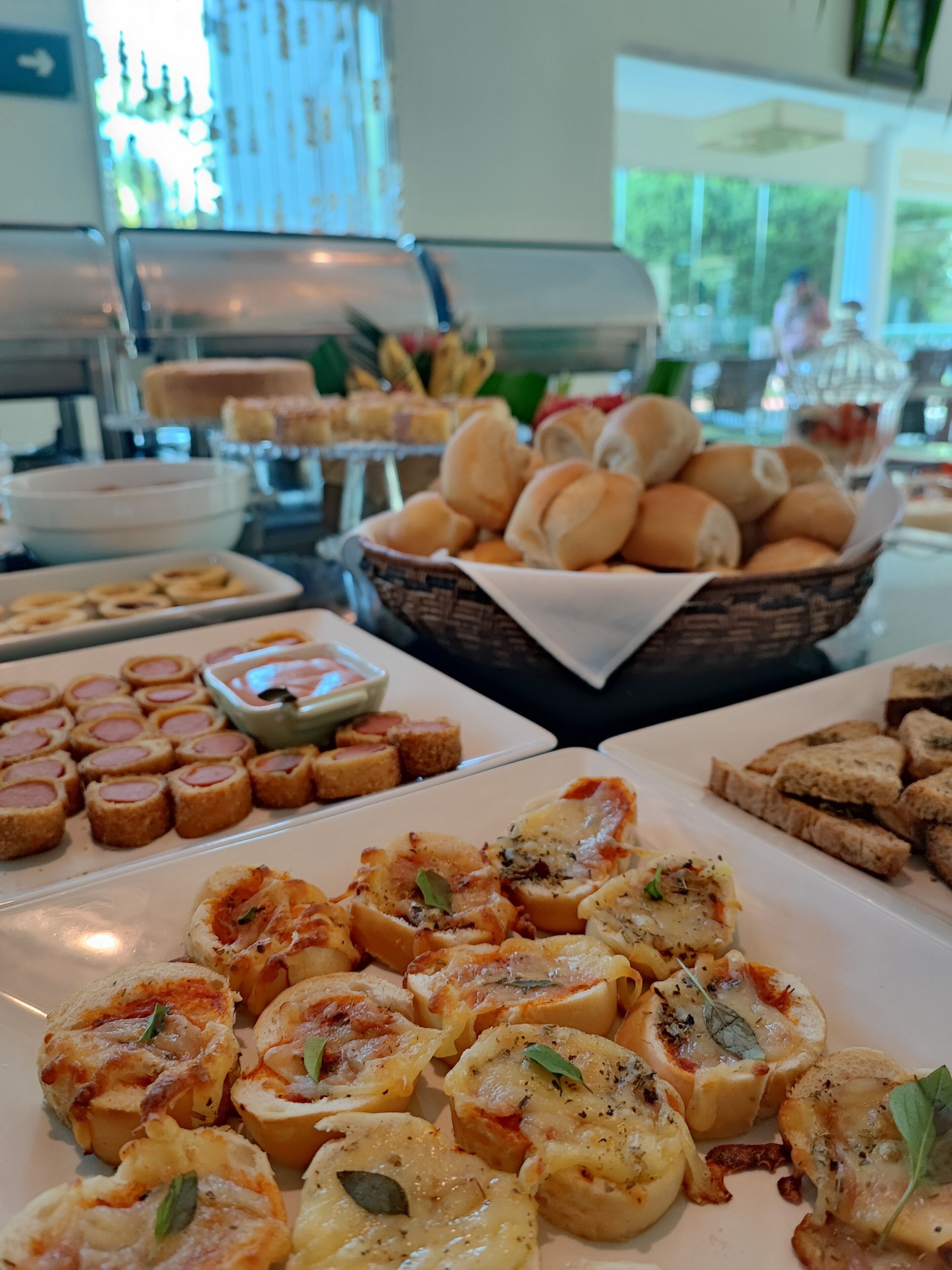 A buffet with various food items including bread rolls, cheese rolls, and sliced bread.