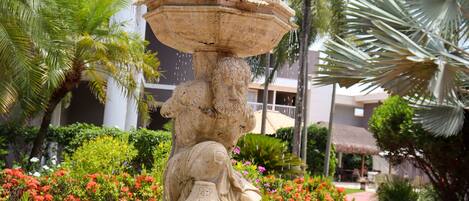 A stone fountain with water spouting from its center, surrounded by vibrant red flowers and lush greenery.