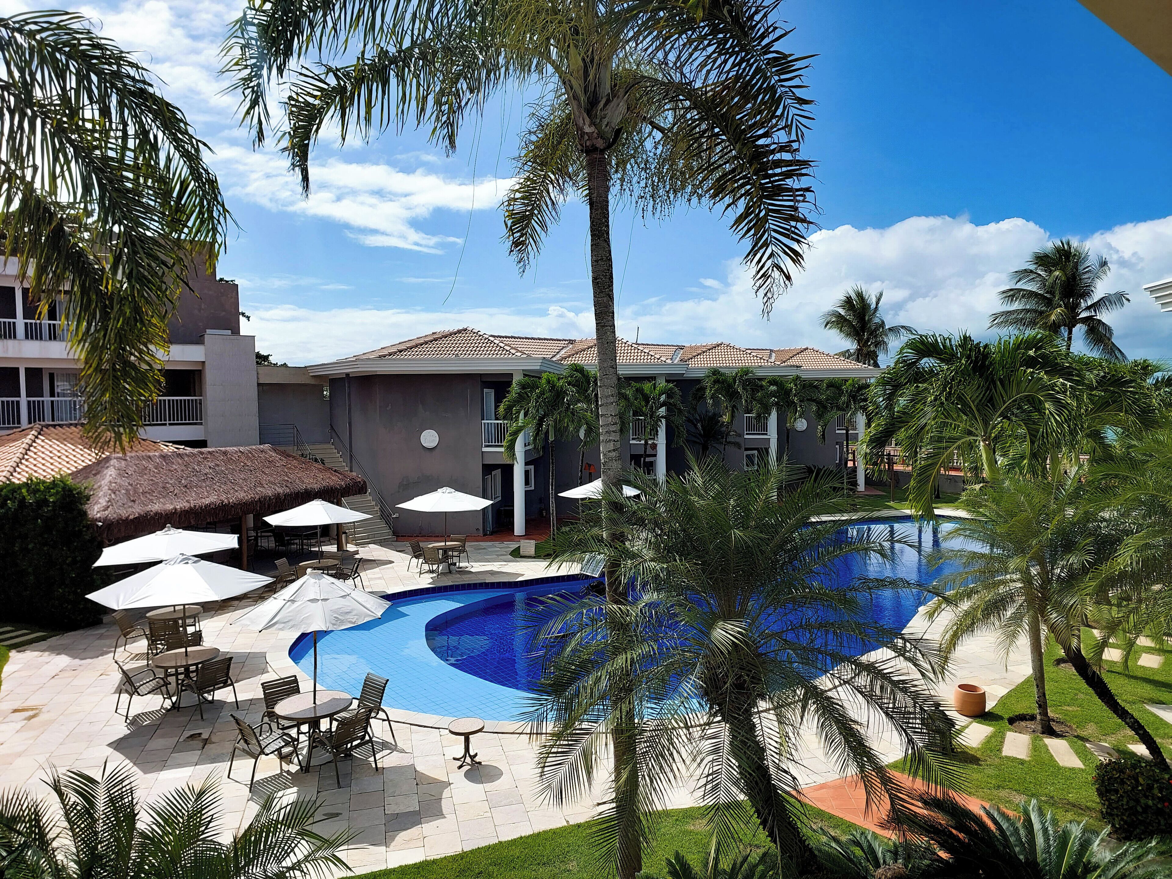 A swimming pool surrounded by palm trees and outdoor seating with umbrellas.