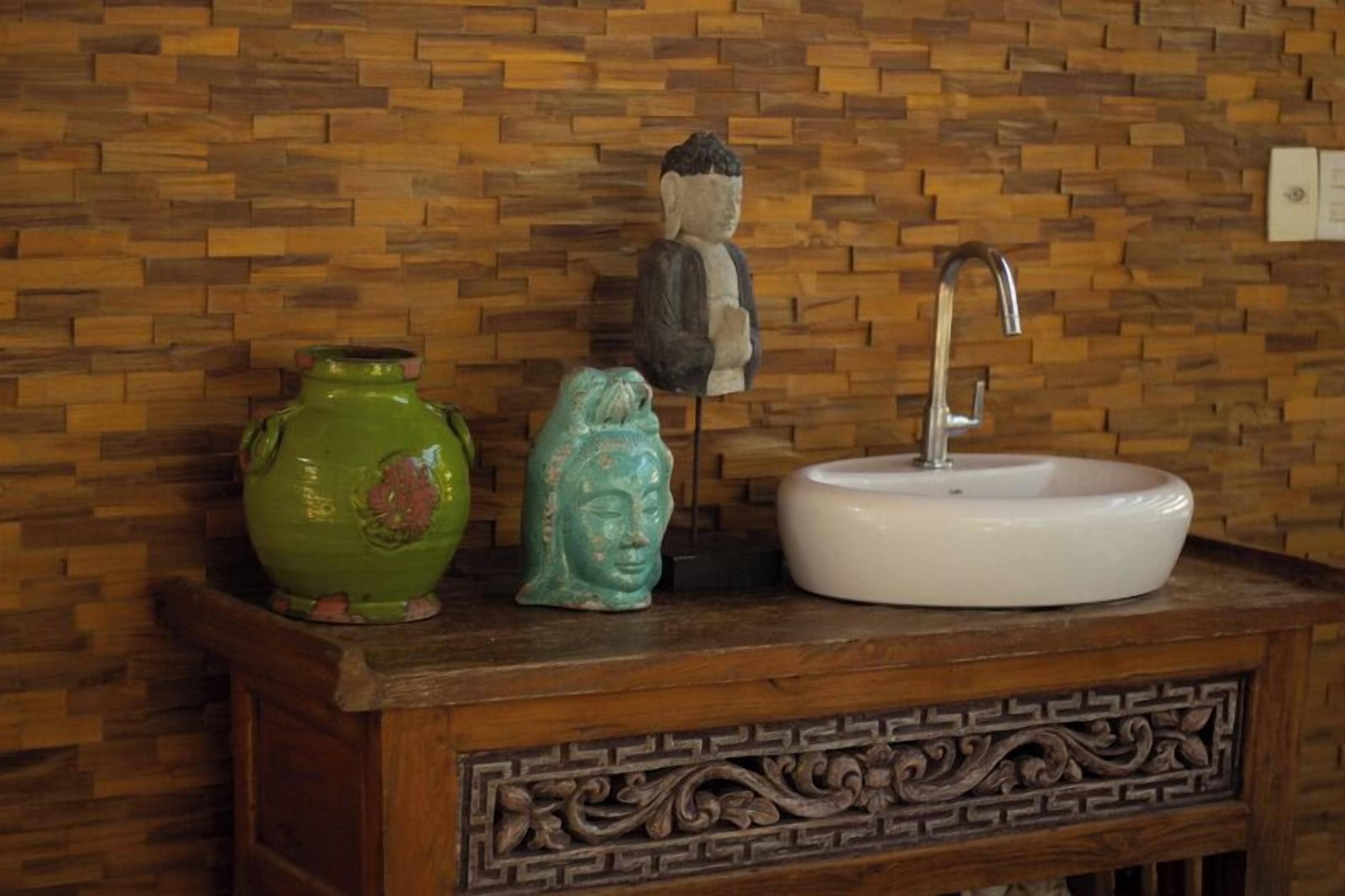 A bathroom vanity with a white sink, a green vase, and a Buddha statue.