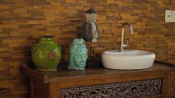 Un tocador de baño con un lavamanos blanco, un jarrón verde y una estatua de Buda.