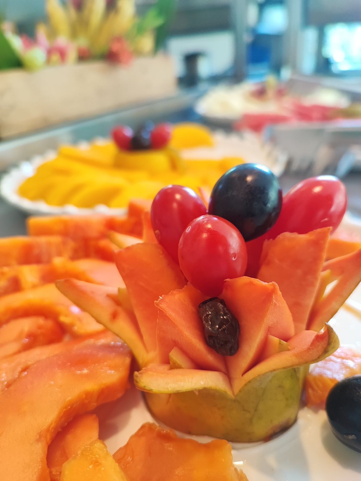A fruit platter with sliced mangoes, tomatoes, and a decorative arrangement of mango slices and a cherry.