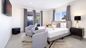 Une chambre d’hôtel moderne avec un grand lit, deux fauteuils, une table de chevet avec une lampe et un téléviseur fixé au mur.