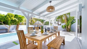 Un espace extérieur abrité, aménagé pour les repas, avec une piscine, des meubles en bois et des plantes tropicales.