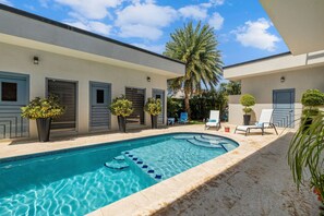 A swimming pool with steps leading into it, surrounded by lounge chairs and potted plants. - Magical Oasis 6BR w Large Pool Gazebo Views (Noord)