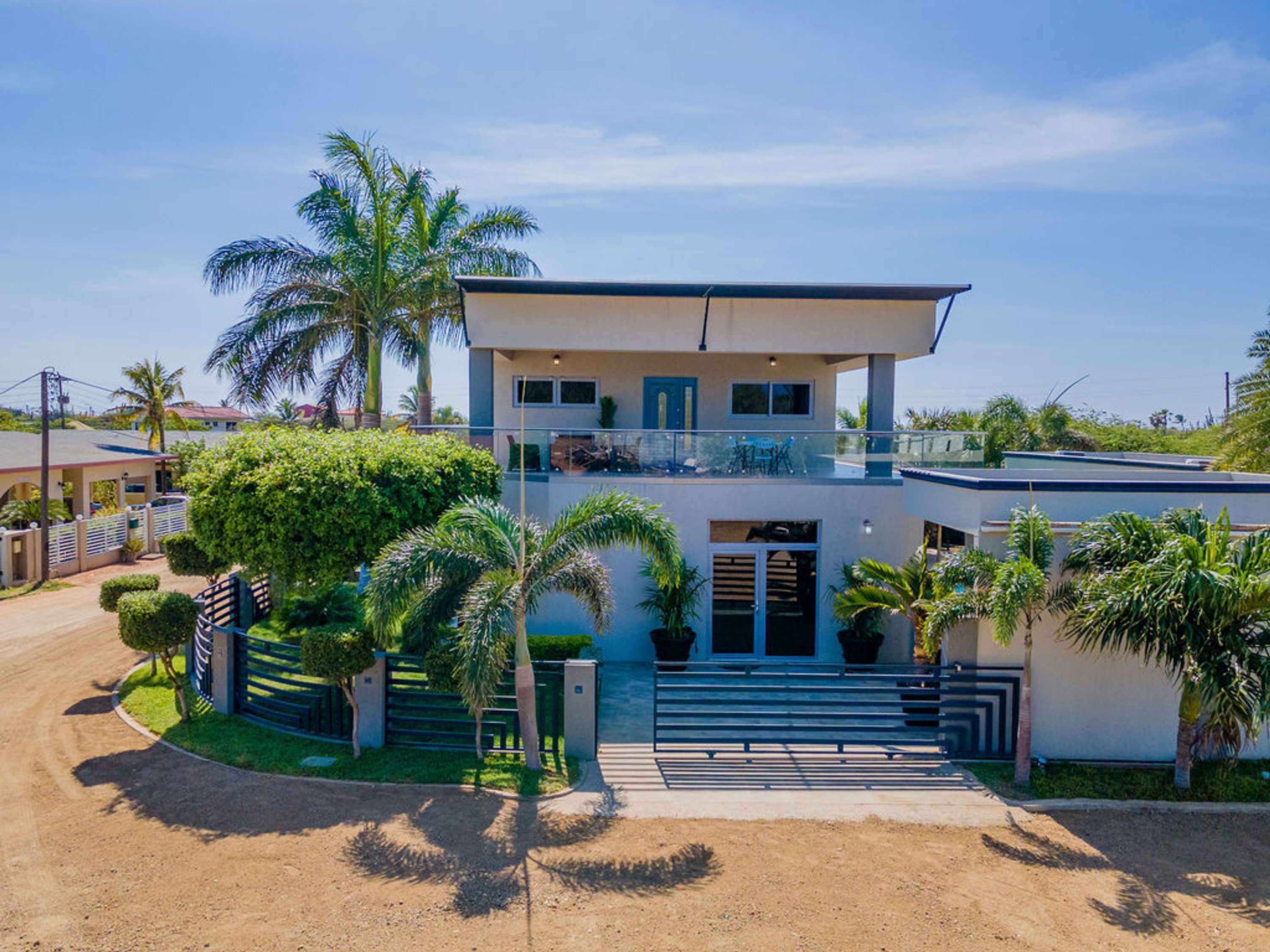 A two-story house with a balcony, surrounded by palm trees and a well-maintained lawn.