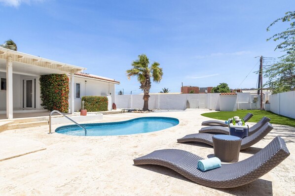 A swimming pool with lounge chairs, a palm tree, and a white building with a garden. - 4br4ba w Private Pool Walking Distance to Ritz (Noord)