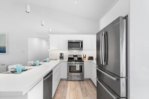 A modern kitchen with white cabinetry, stainless steel appliances, and a central island with blue glassware.