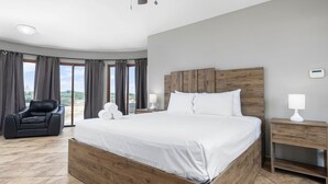 A modern hotel room with a large bed, a leather chair, a nightstand, and a view of the outdoors. - Amazing 4br4ba Villa w Pool Birdsanctuary Views (Noord)