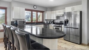 A modern kitchen with a central island, stainless steel appliances, and a clock on the wall. - Amazing 4br4ba Villa w Pool Birdsanctuary Views (Noord)