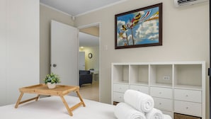 A hotel room with a bed, a wooden side table with a plant, a painting on the wall, and a white dresser with towels. - Lovely 3br2ba w Wifi Parking in Central Location (Paradera)