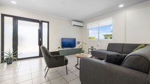 A modern living room with a grey sofa, a black armchair, a small coffee table, a flat-screen TV, and a potted plant. - Lovely 3br2ba w Wifi Parking in Central Location (Paradera)