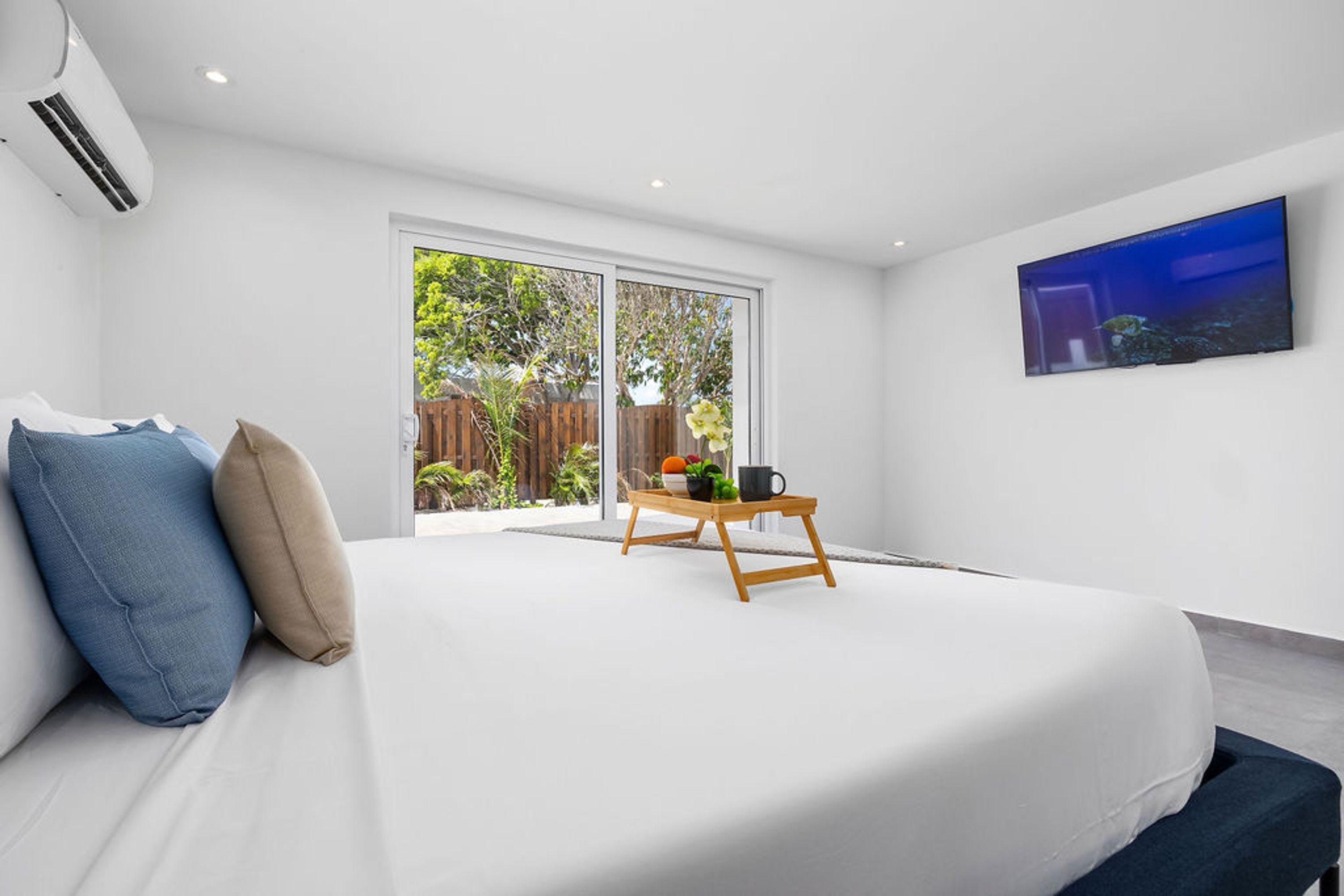 A modern bedroom with a large bed, a wooden bedside table, and a TV on the wall.